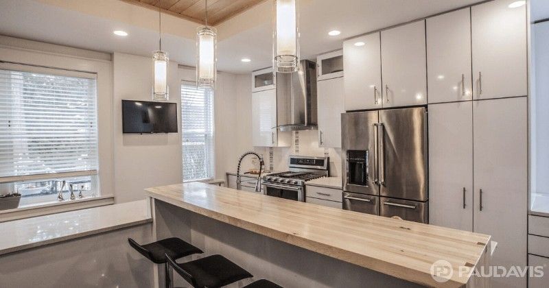 Modern kitchen with light wood countertop, stainless steel appliances, and hanging pendant lights.