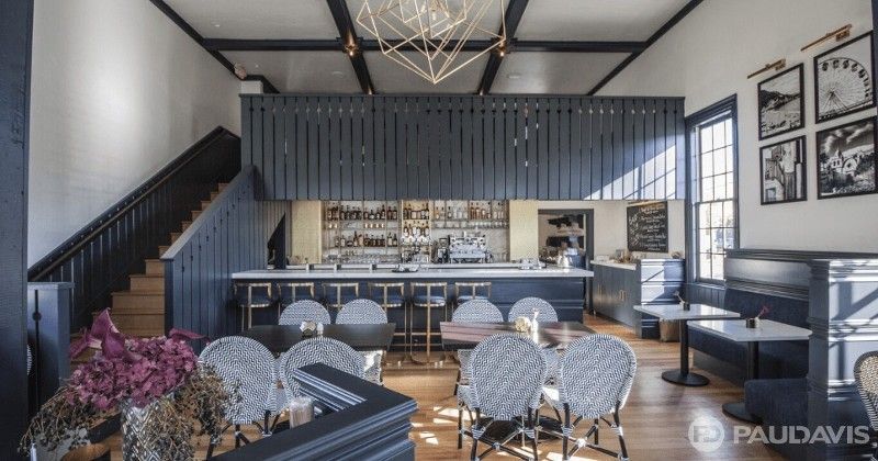 Interior of a restaurant with a bar, seating, and staircase. Dark blue and white color scheme, light fixtures.