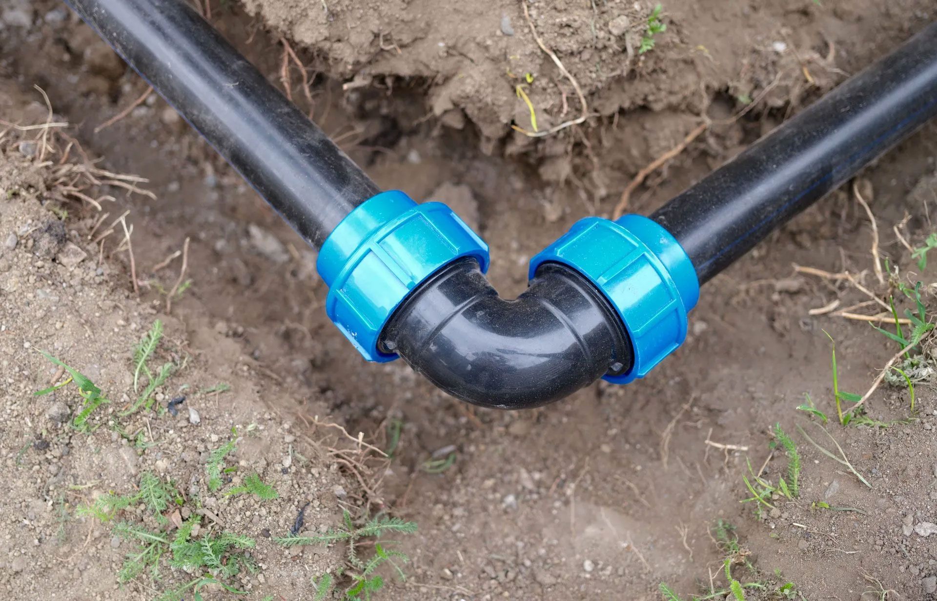 Two black pipes with blue connectors are connected to each other in the dirt.