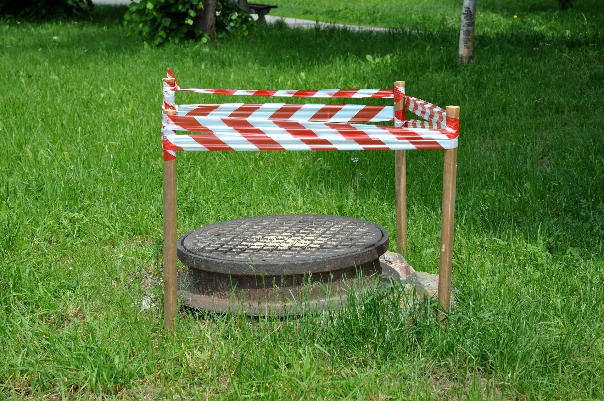 A manhole cover is surrounded by a red and white striped tape.