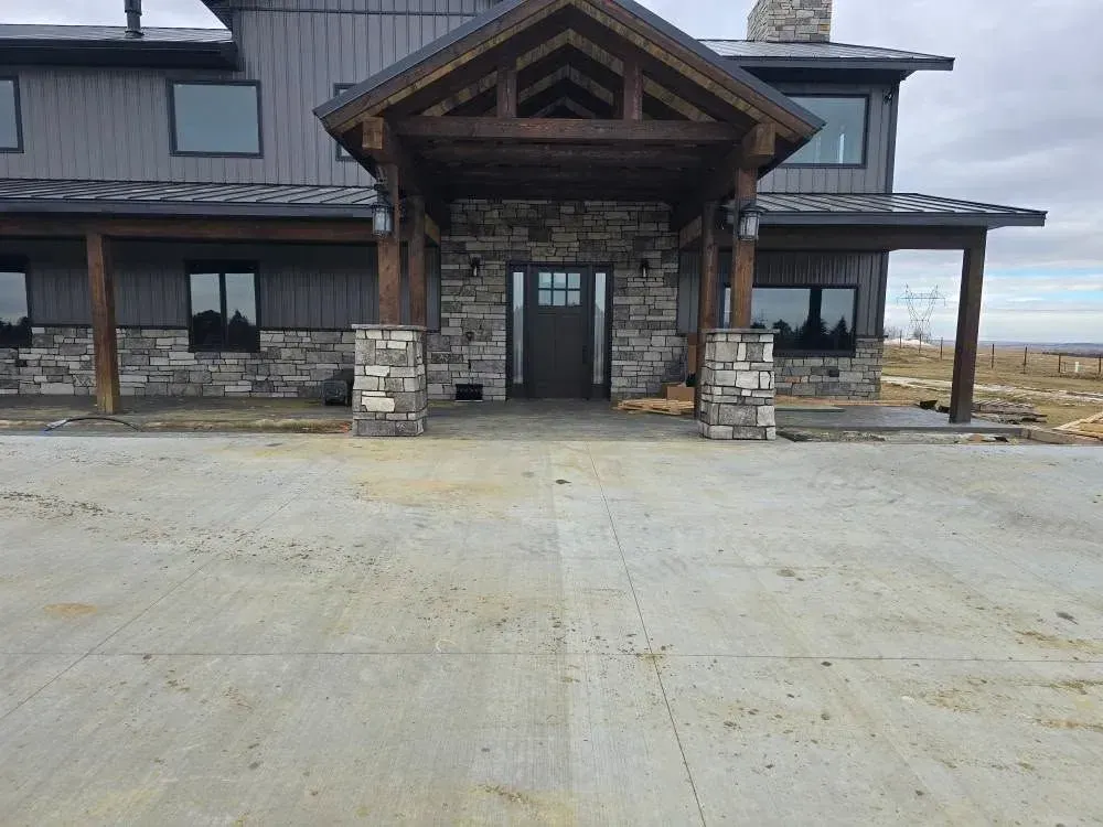 Large gray house with stone entryway and wooden accents; concrete driveway.