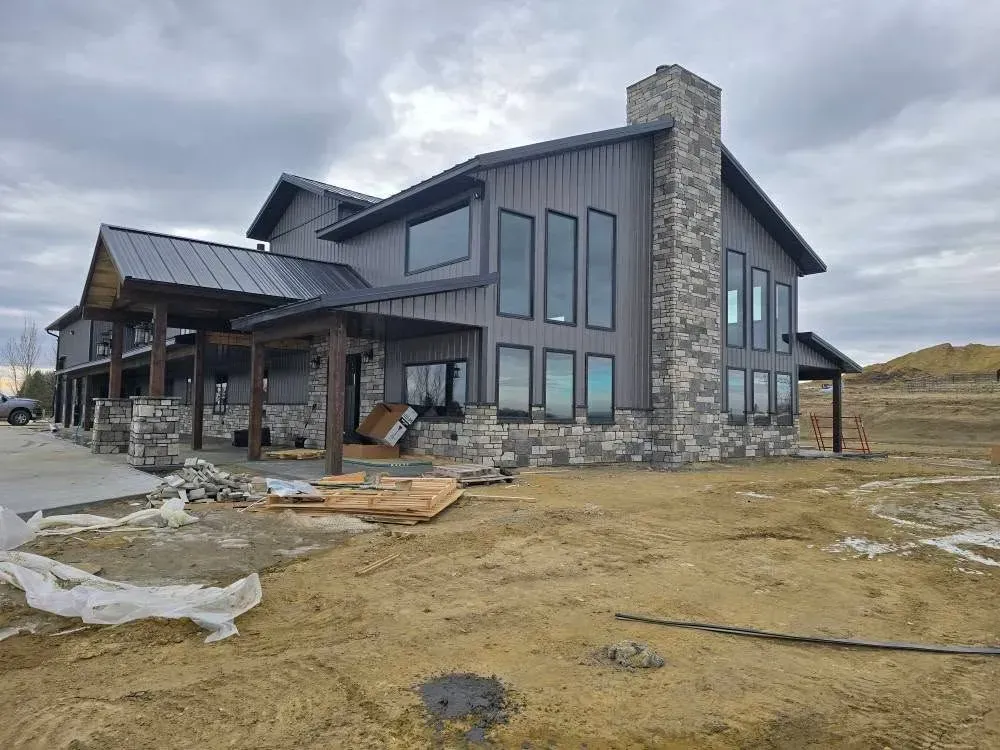 Modern two-story house with stone and dark siding, large windows, and chimney on a cloudy day.