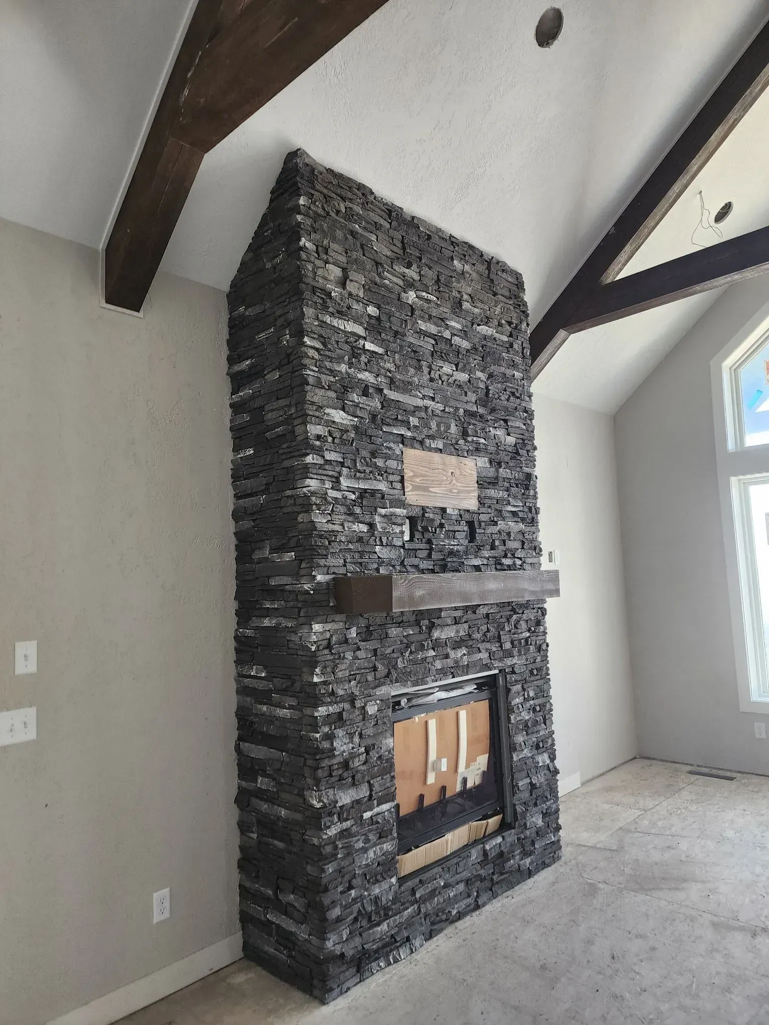 Stone fireplace with wooden mantle and beams, in a room with a vaulted ceiling.
