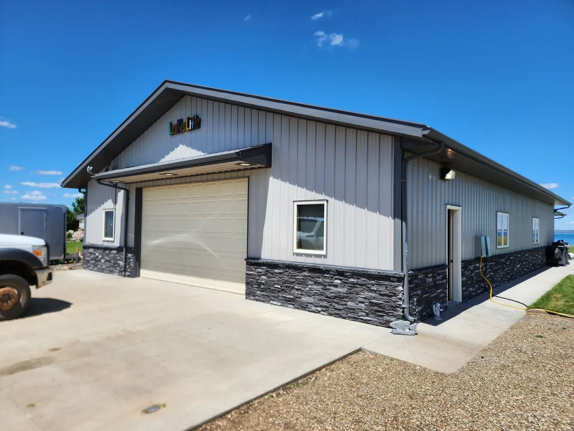 Metal building with large garage door, stone base, and sign under a bright blue sky.
