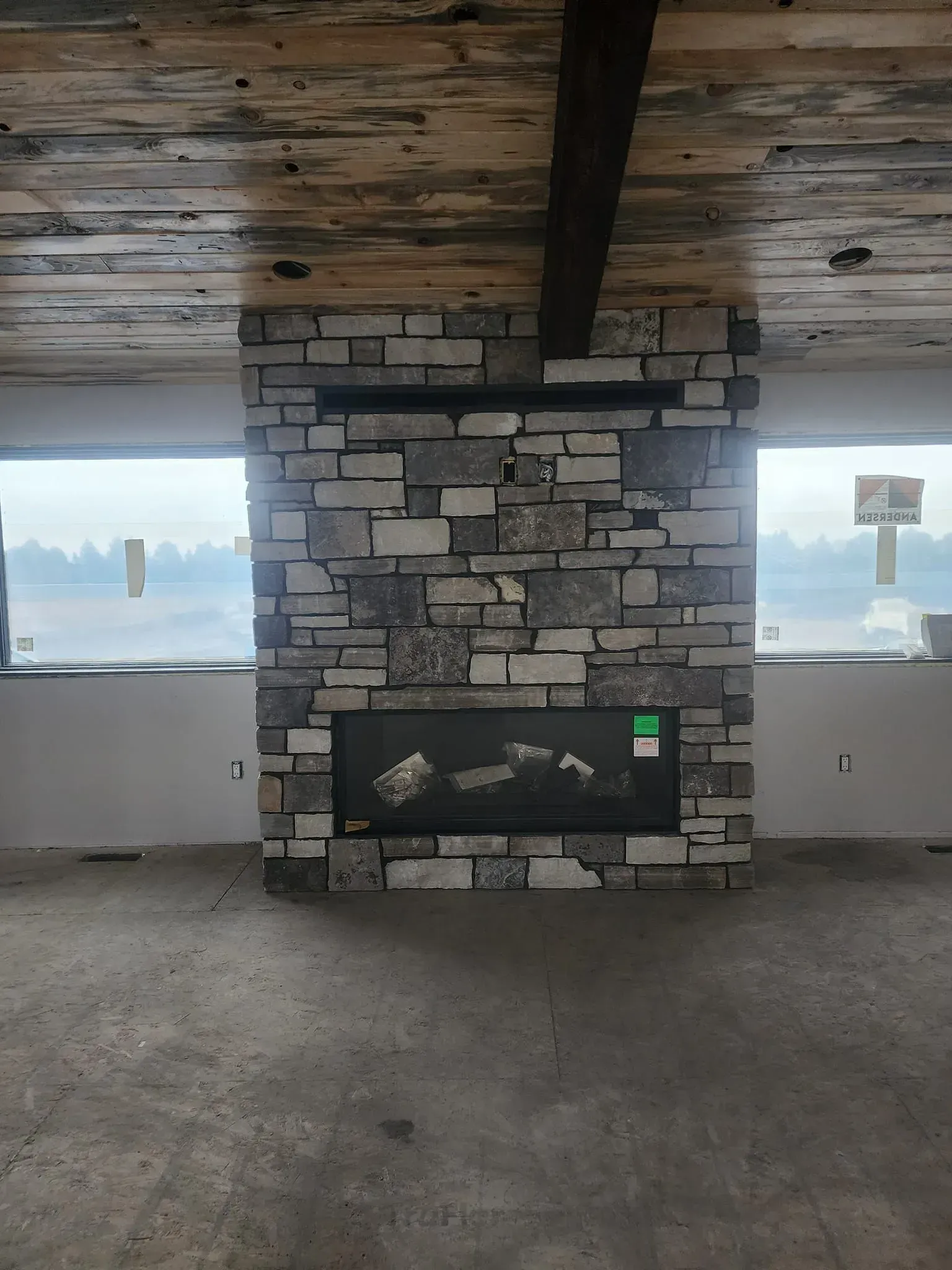 Stone fireplace with recessed electric fireplace, in a room with unfinished walls and ceiling.