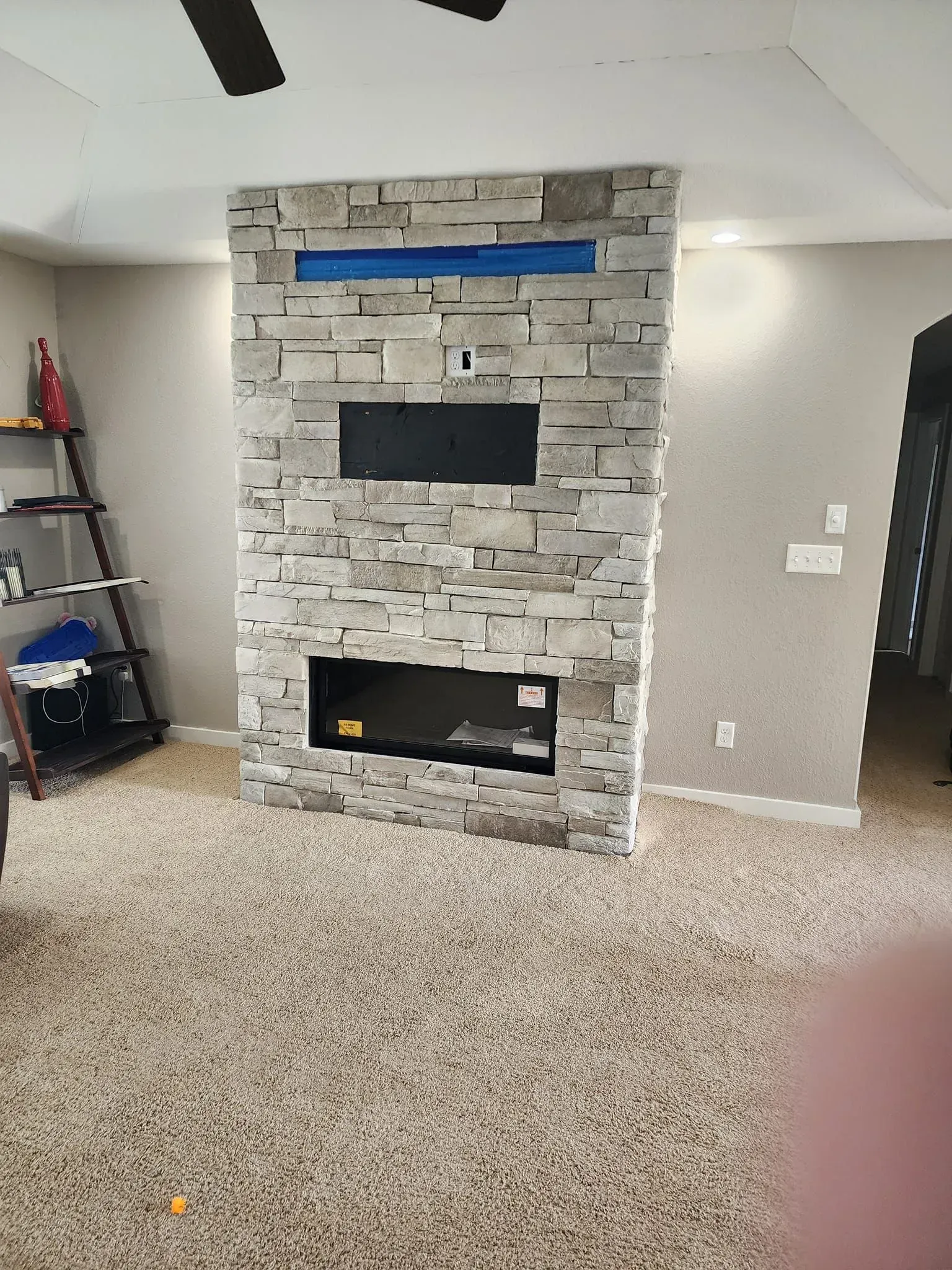 Stone-faced fireplace with built-in TV and storage against a neutral wall; carpeted floor.