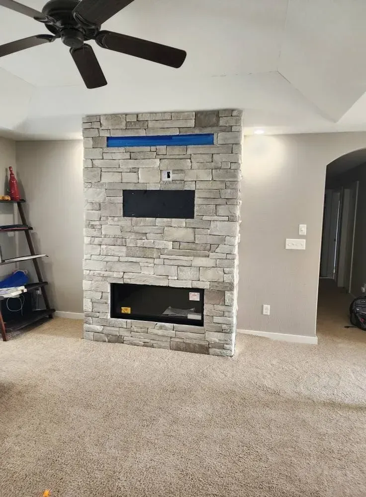 Stone accent wall with built-in fireplace and media space, gray walls and beige carpet.