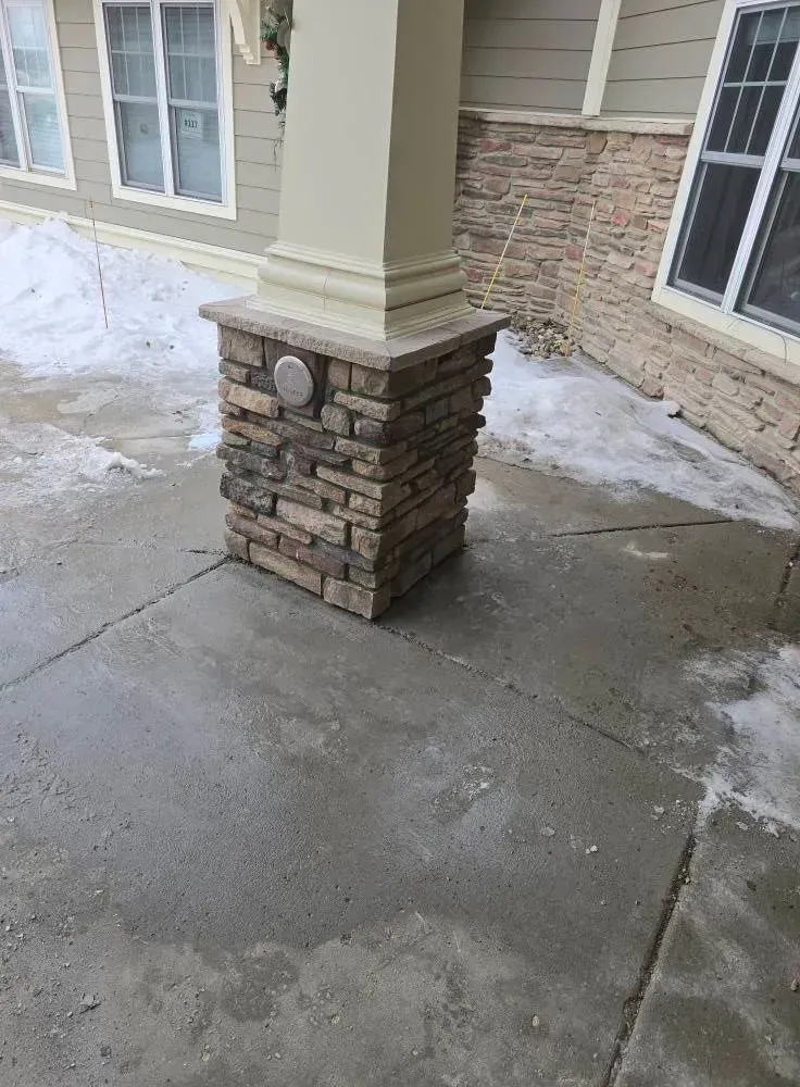 Stone pillar base supporting a cream-colored column on a concrete porch, with snow visible.