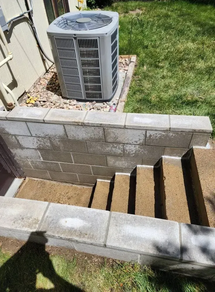 Concrete block steps descend into a basement entrance with an air conditioning unit above.