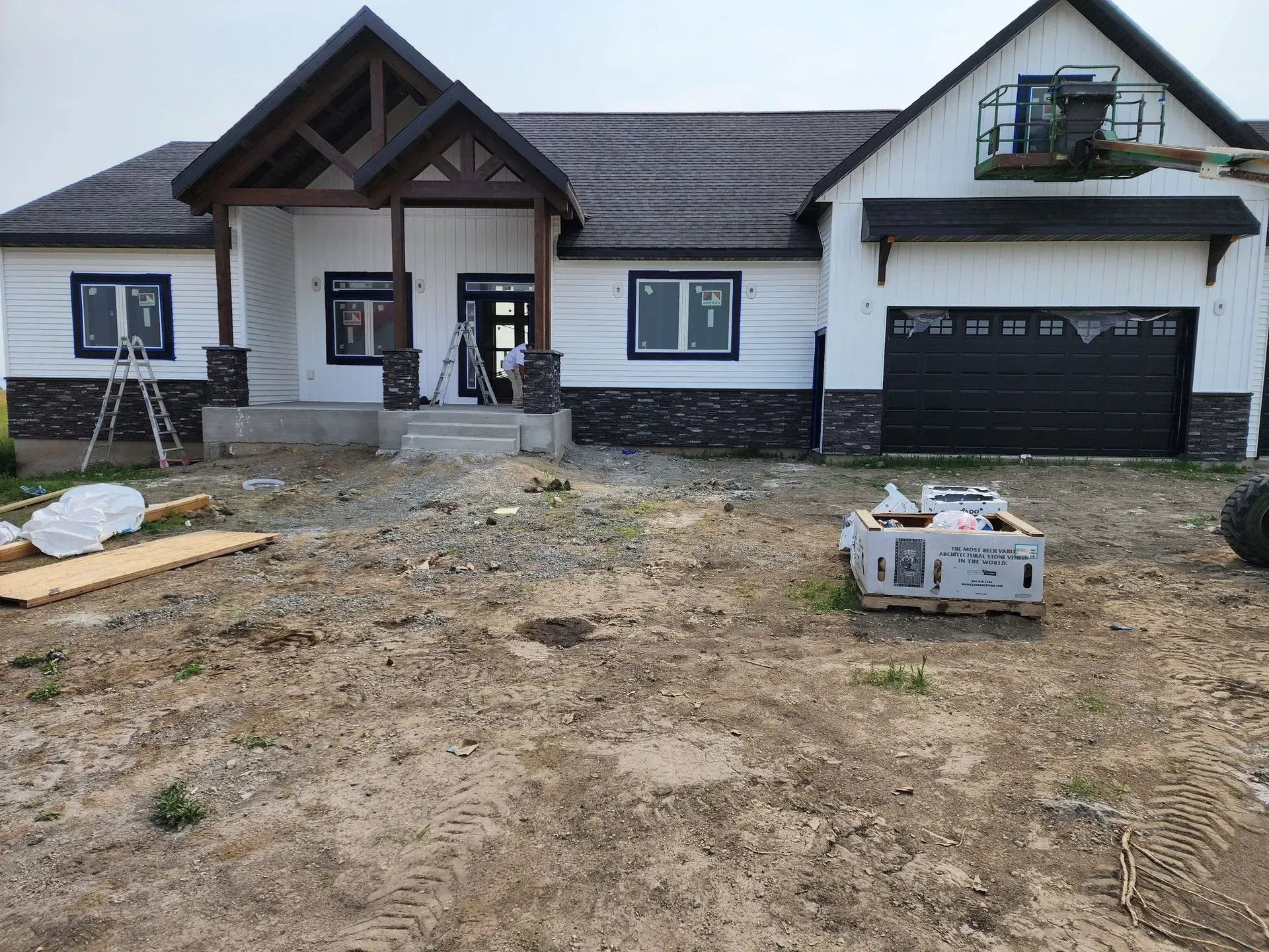 New house exterior under construction, white siding, dark trim, black garage door, brown brickwork, and a lift.