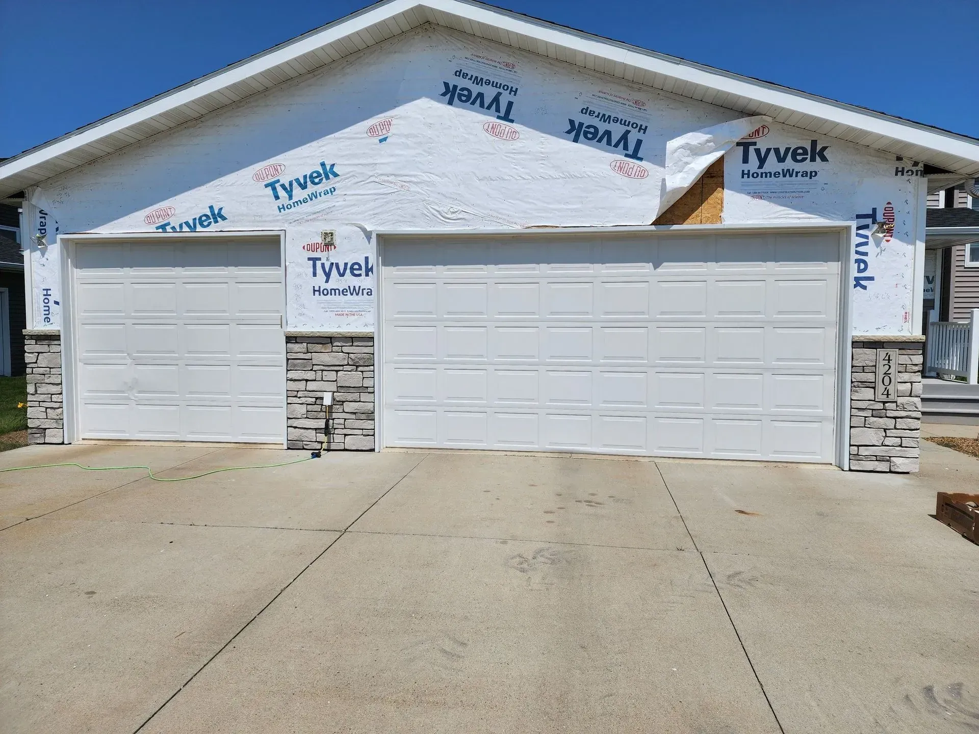 Two-car garage with white doors, stone accents, and Tyvek wrap. Concrete driveway in front.