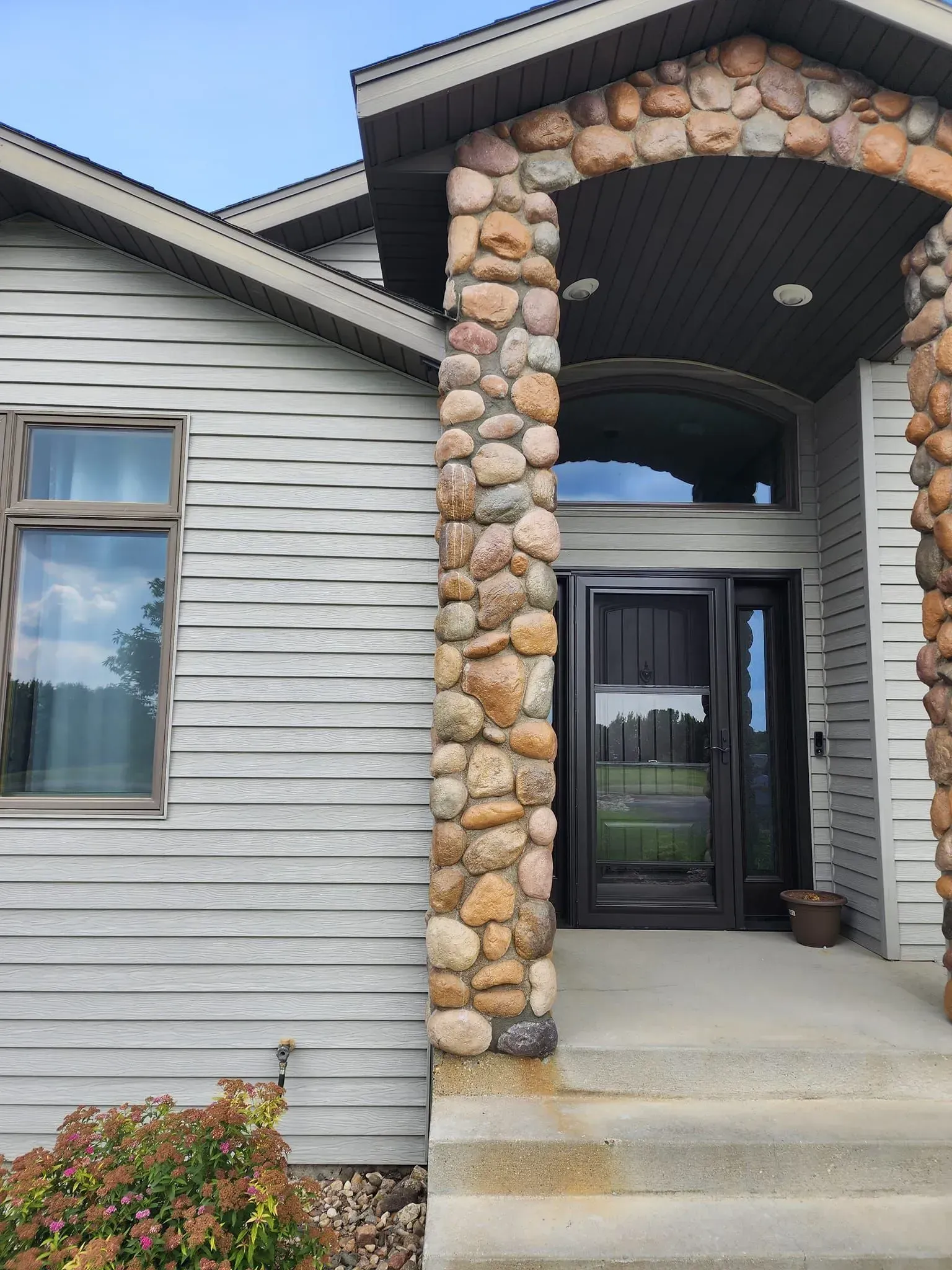 Stone-pillared home entrance with a gray door. Window to the left, stone arch above the door. Concrete steps.