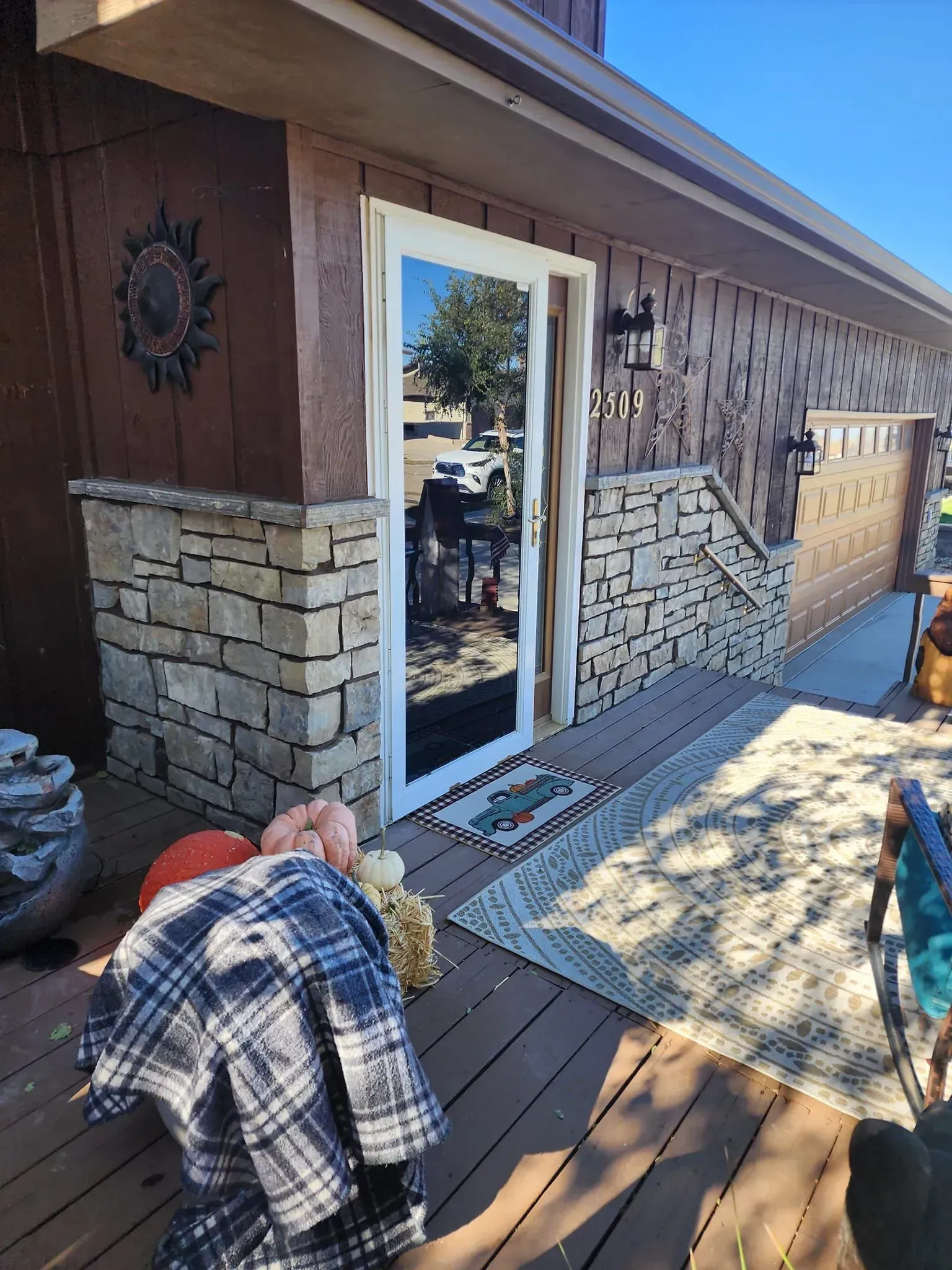 Front porch with a stone facade. A glass door reflects the outdoors. Flannel shirt and pumpkins rest on the porch.