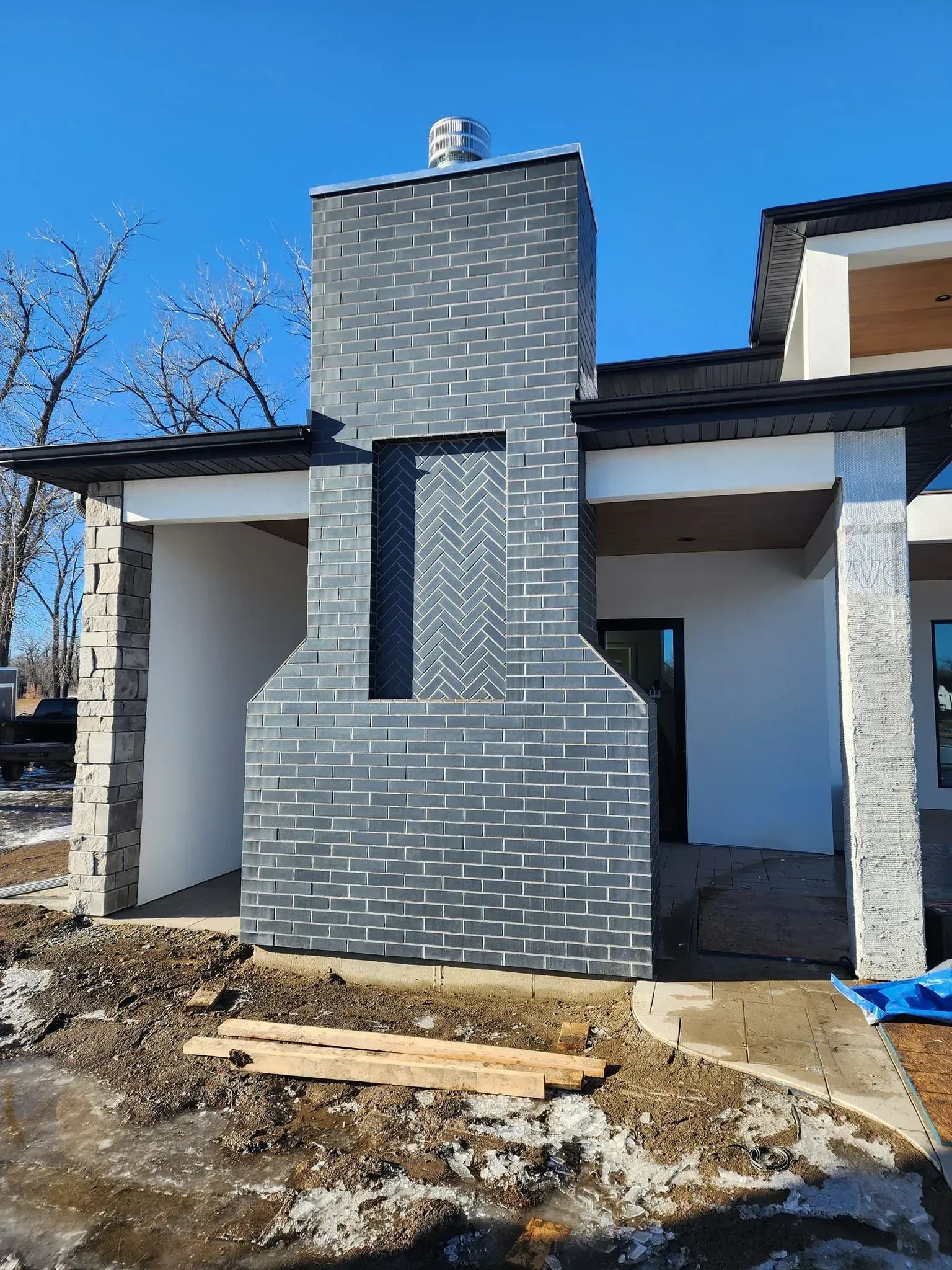 Exterior brick chimney on a house under construction. Blue-gray bricks with white accents. Clear sky.