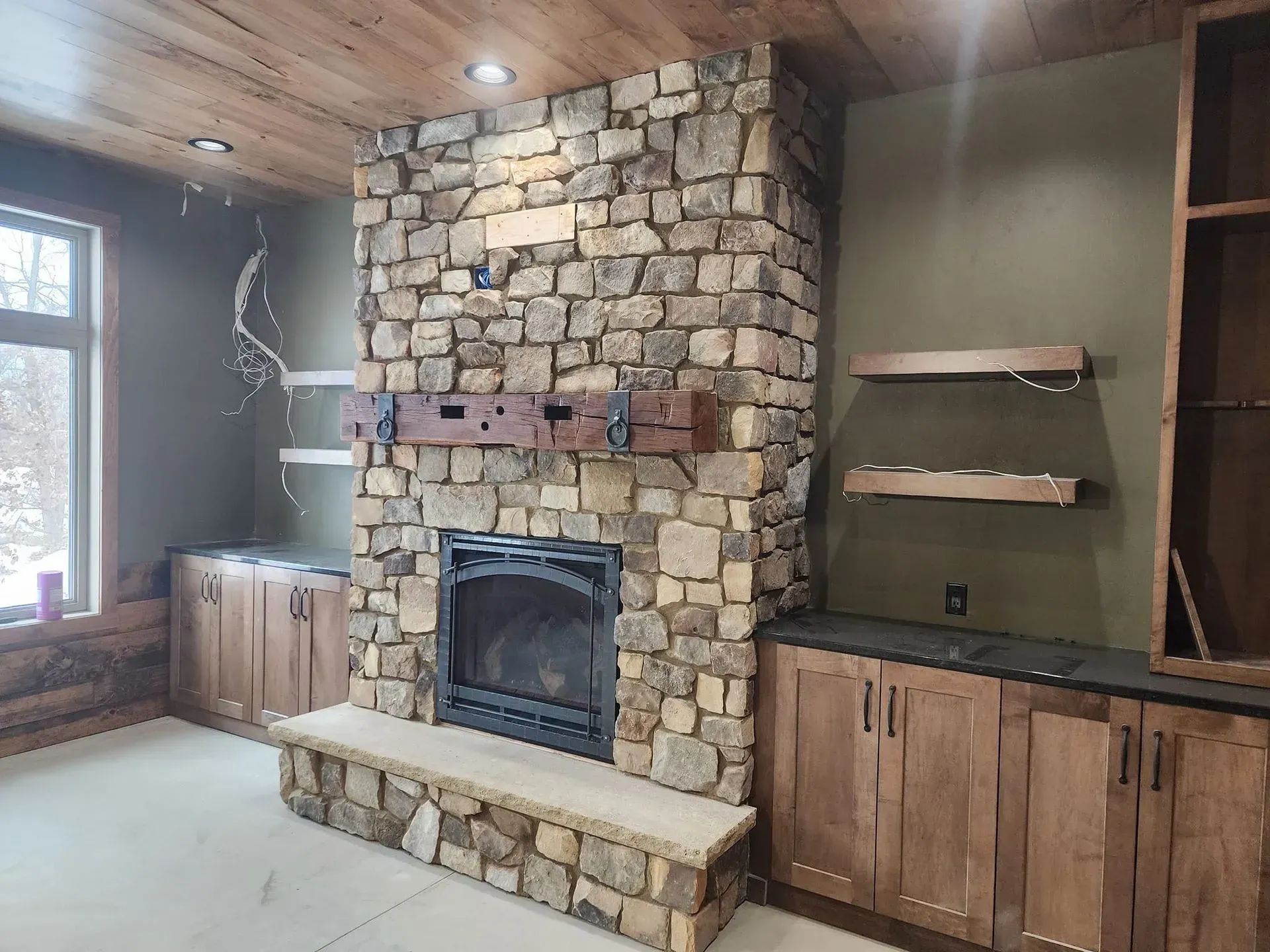 Stone fireplace with wooden mantel and built-in cabinets in a room with light-colored walls and ceiling.