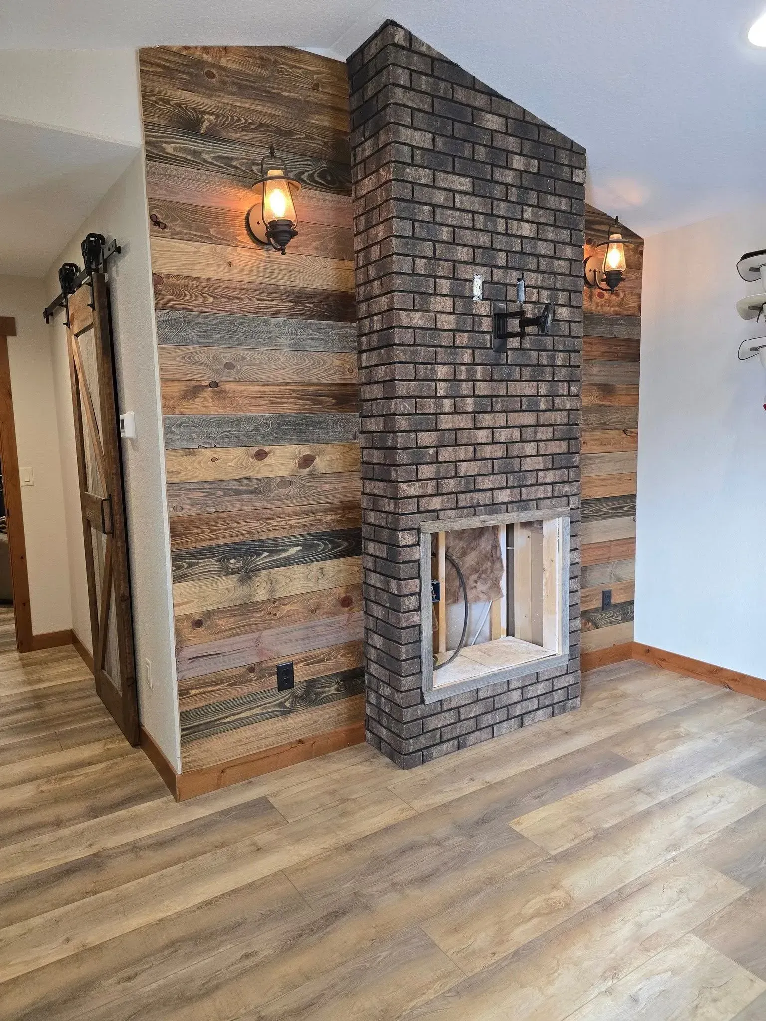 Fireplace with brick and wood accents, sconce lighting, and a barn door.