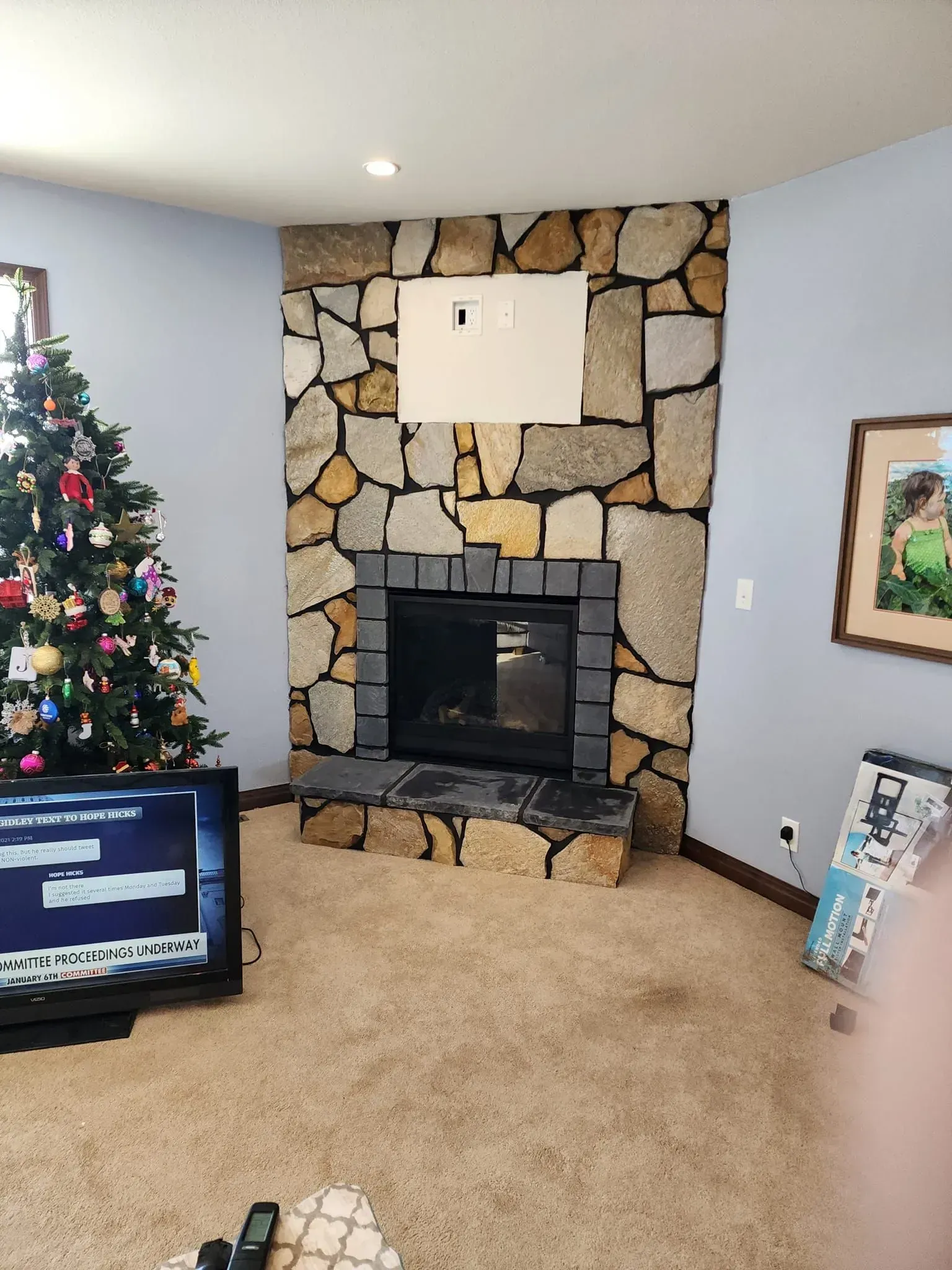 Stone fireplace with a black fireplace insert, next to a Christmas tree and a TV.
