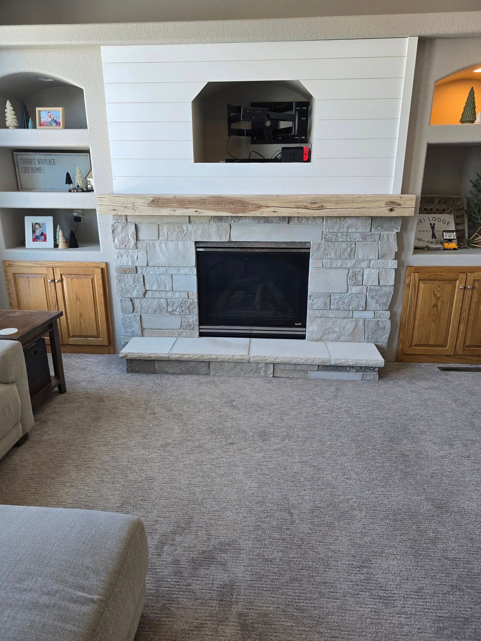 Living room with stone fireplace, wood mantel, built-in shelving, and a mounted TV.