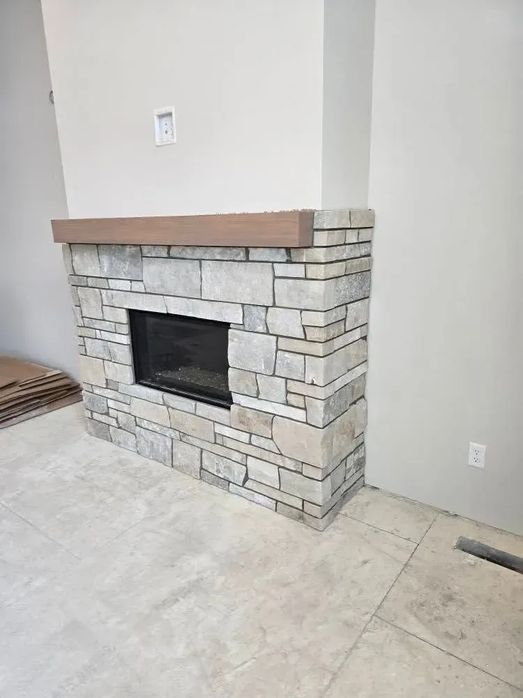 Stone-clad fireplace with dark insert, light wood mantel, and light-colored walls.