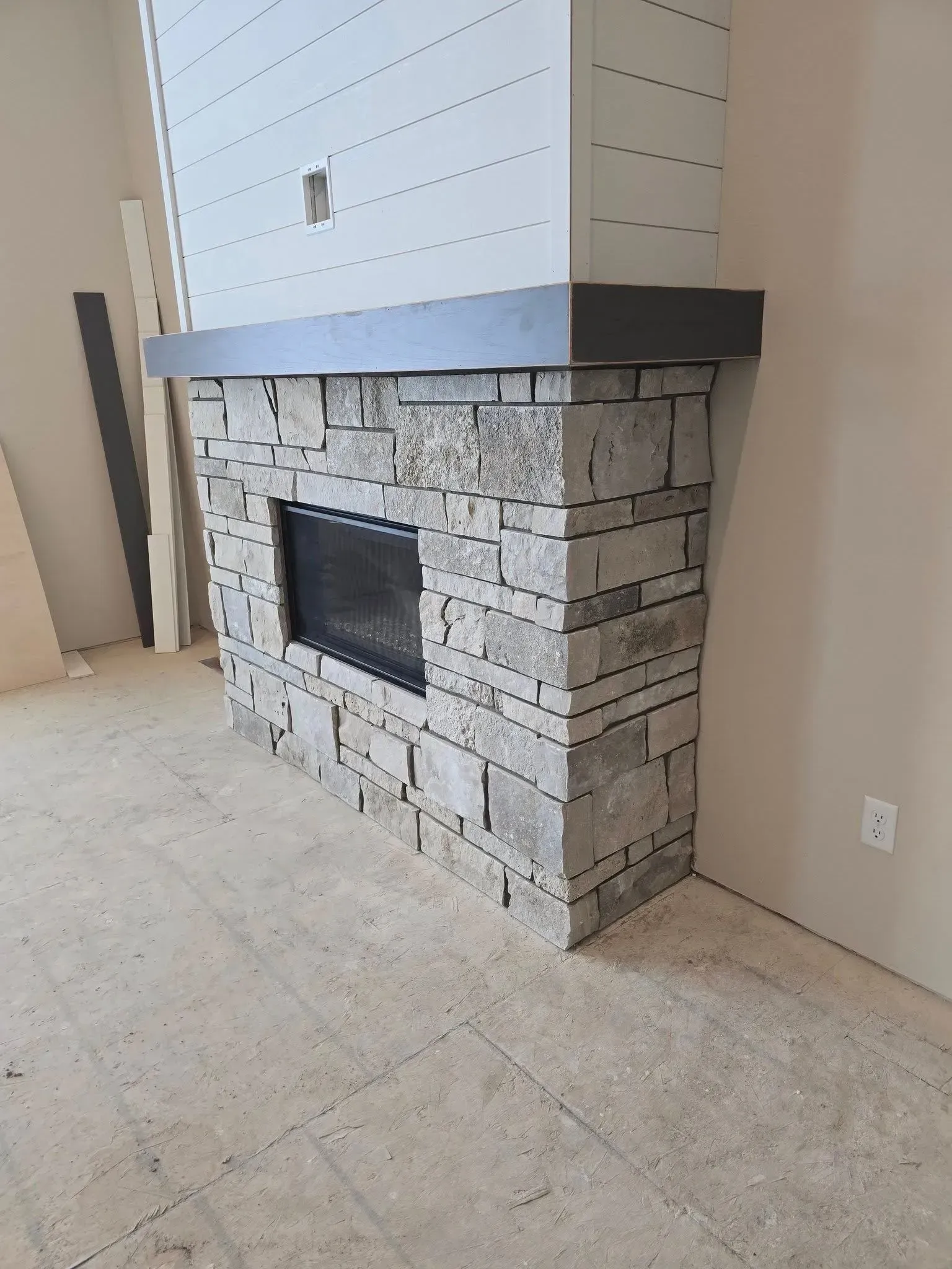 Stone fireplace with black interior and gray and white details, in a room under construction.