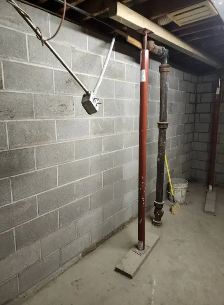Basement with concrete block wall, support posts, and plumbing.