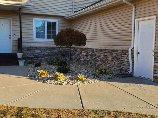 Exterior of house with a stone and tan siding, small tree, and a concrete path.