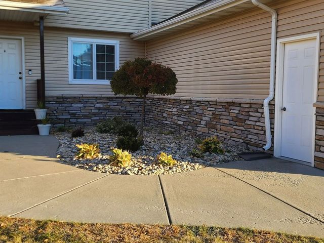 Exterior of house with a stone and tan siding, small tree, and a concrete path.