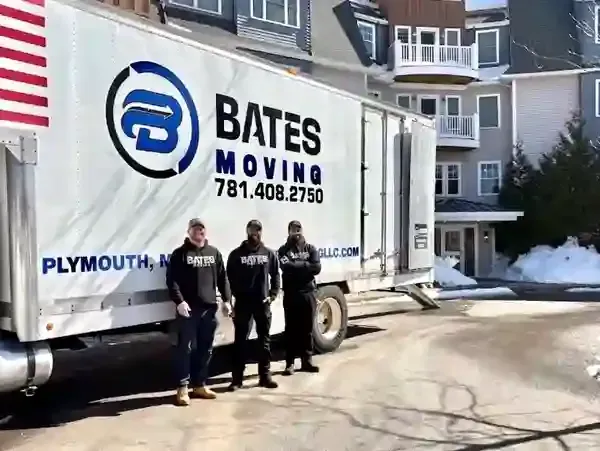 Moving truck with “Bates Moving” logo, two workers standing outside in a snowy driveway.