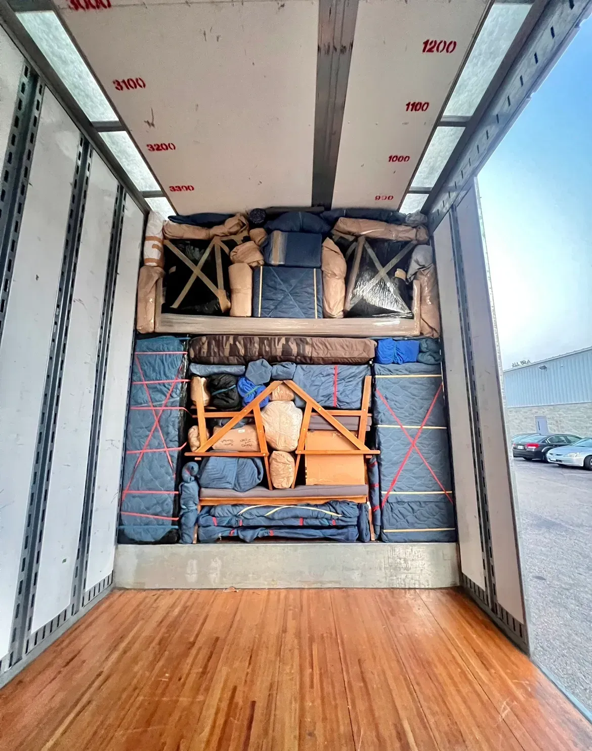Inside a cargo trailer, wrapped machinery and pallets are stacked against the front wall.