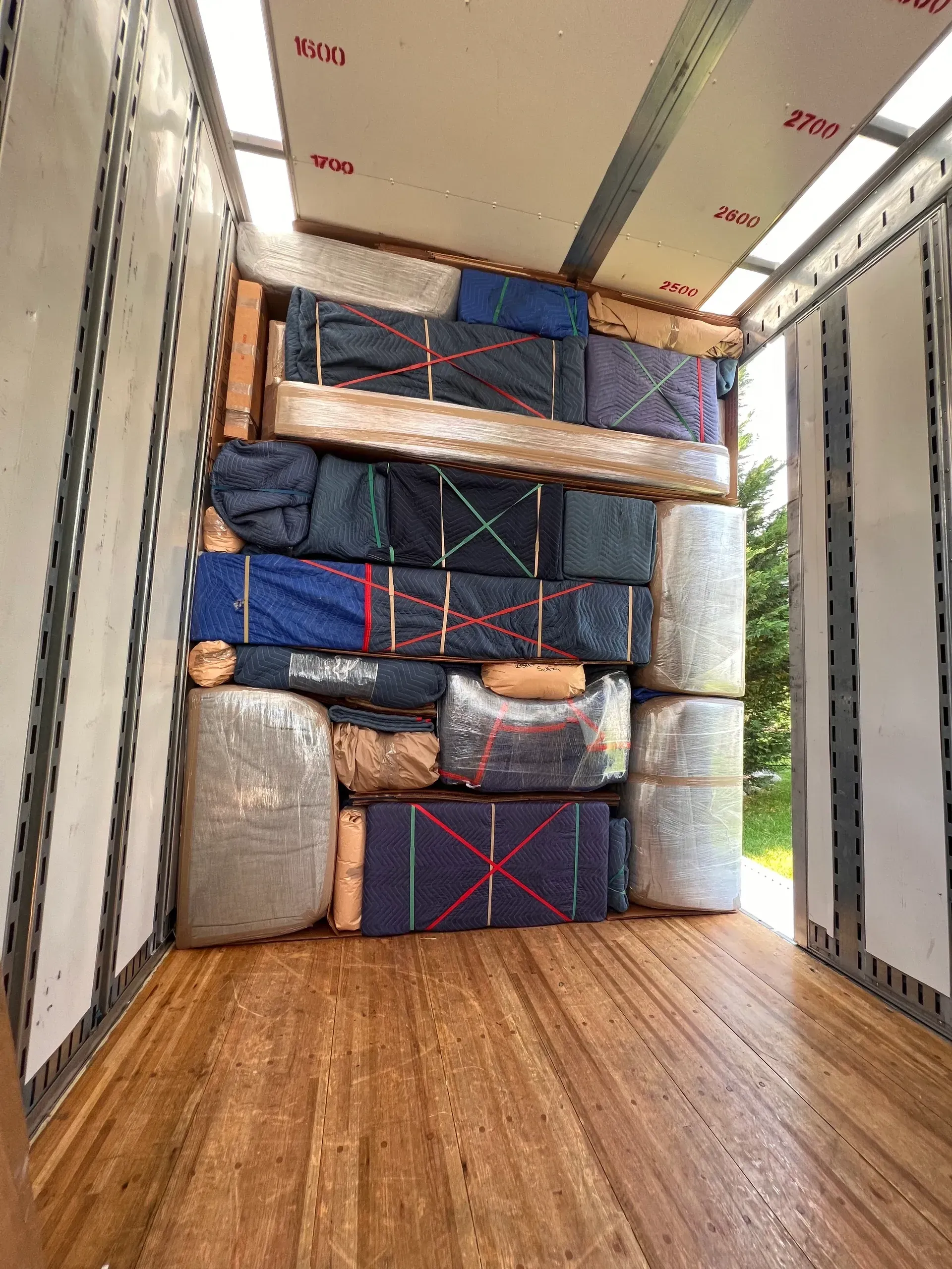 Packed moving truck with stacked mattresses and furniture blocking the cargo area and wooden floor