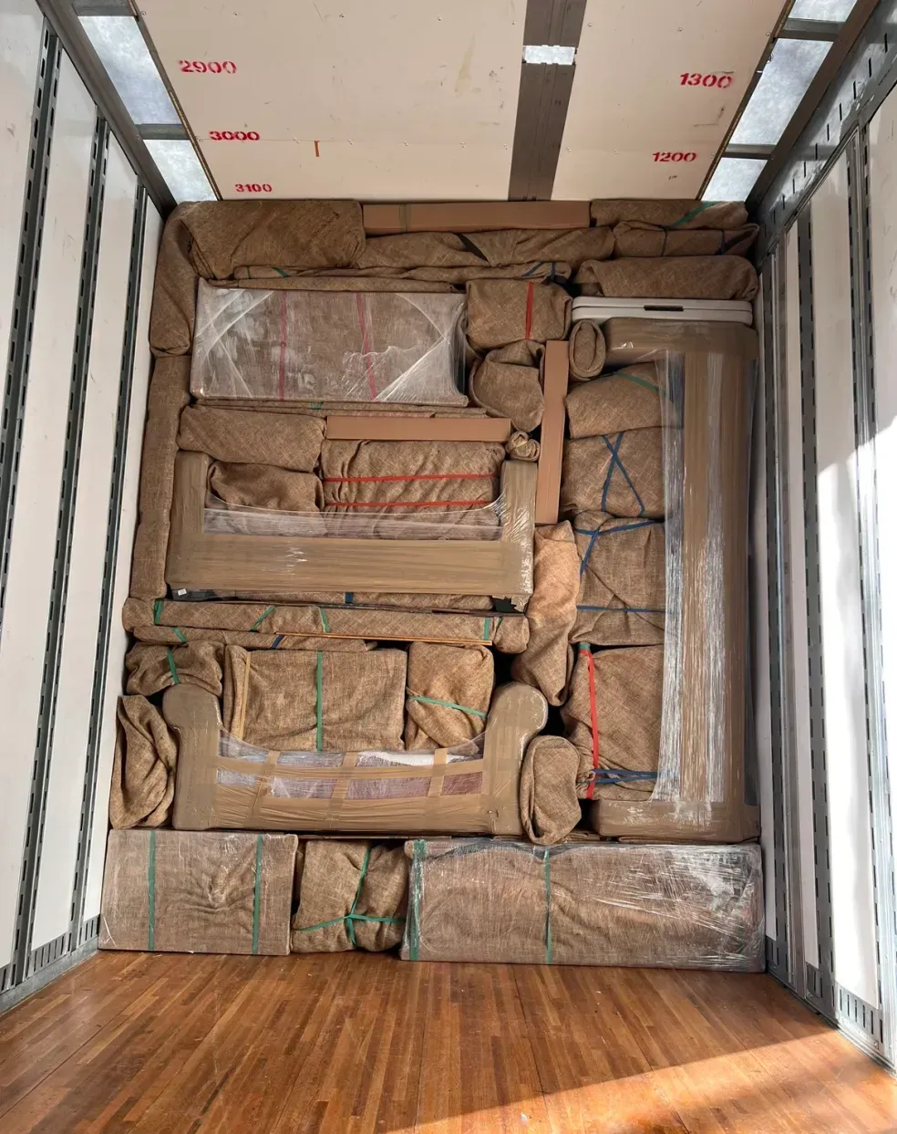 Packed furniture and boxes secured inside a moving truck with brown wrapping and straps