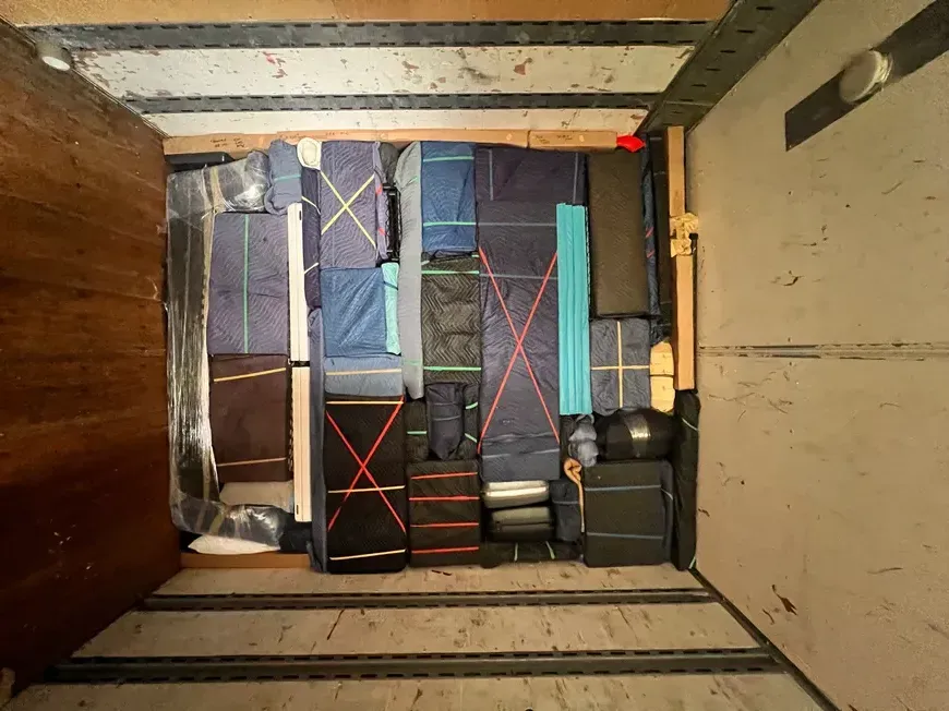 Moving truck cargo area packed with stacked suitcases, bags, and boxes secured with straps.