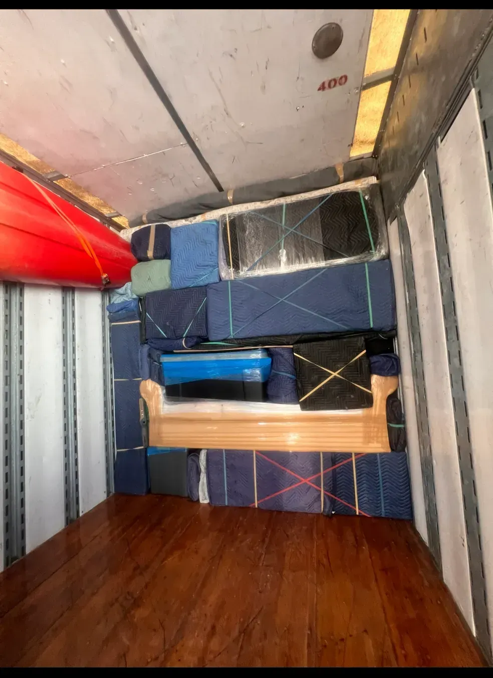 Messy storage room with stacked mattresses, blue bin, wooden floor, and metal shelves