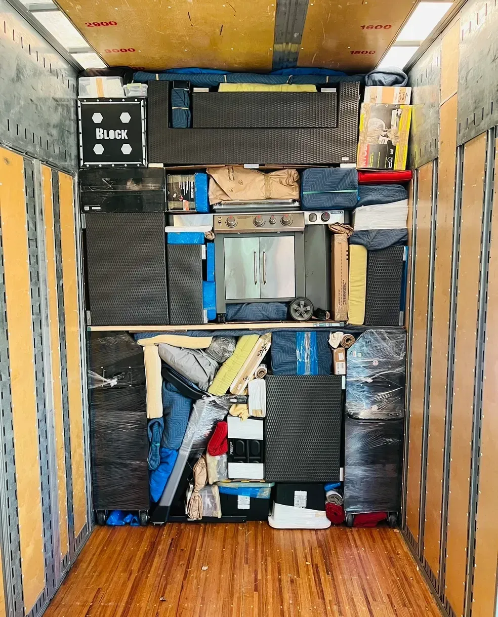 A cluttered storage cabinet with stacked bags, bins, and boxes in a narrow wooden closet.