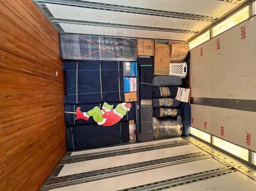 Packed moving truck with boxes, bins, and furniture secured inside a wood-paneled cargo space.