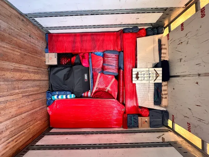 Packed moving truck with red padded furniture, boxes, and bags secured inside.