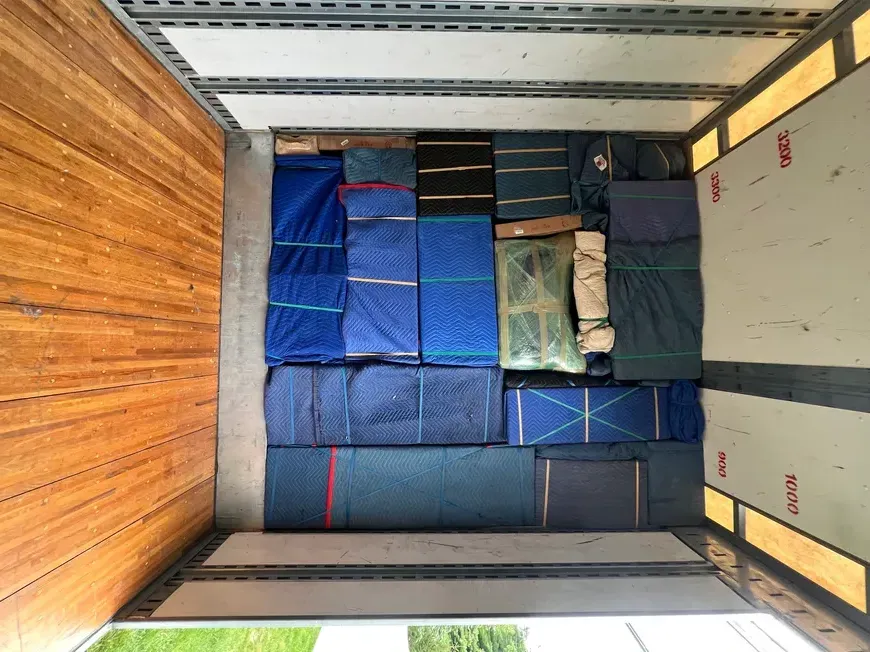 Stacked blue and gray wrapped cargo inside a truck trailer, with wooden side panels visible.