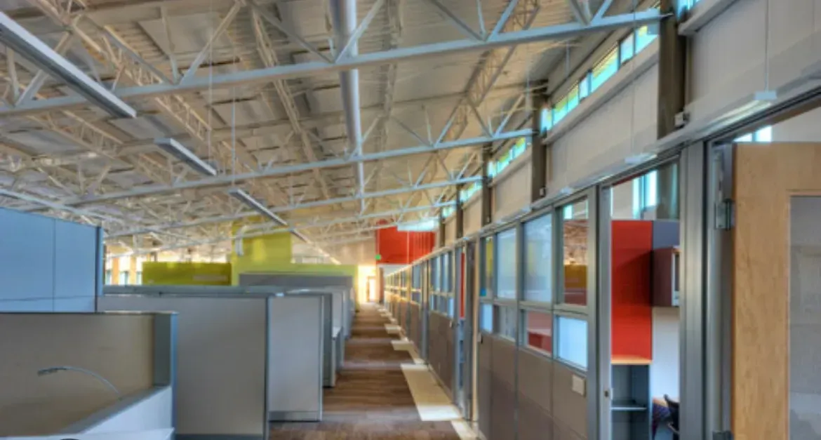 Modern office interior with cubicles, glass-walled rooms, and exposed ceiling beams