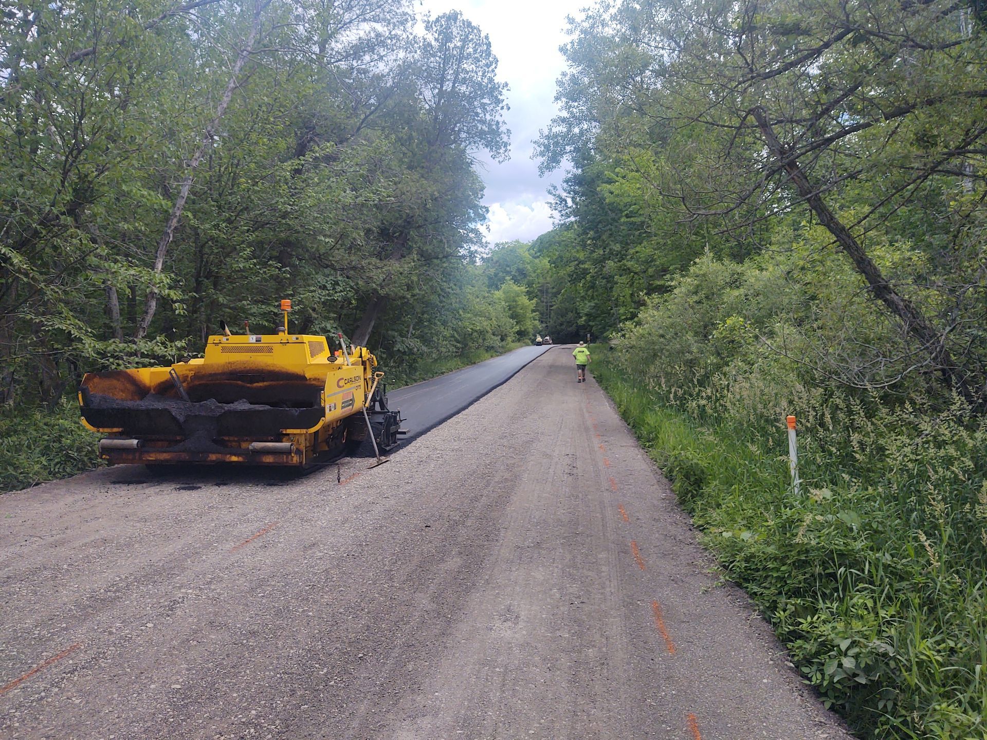 A yellow asphalt paving machine is sitting on the side of a dirt road.