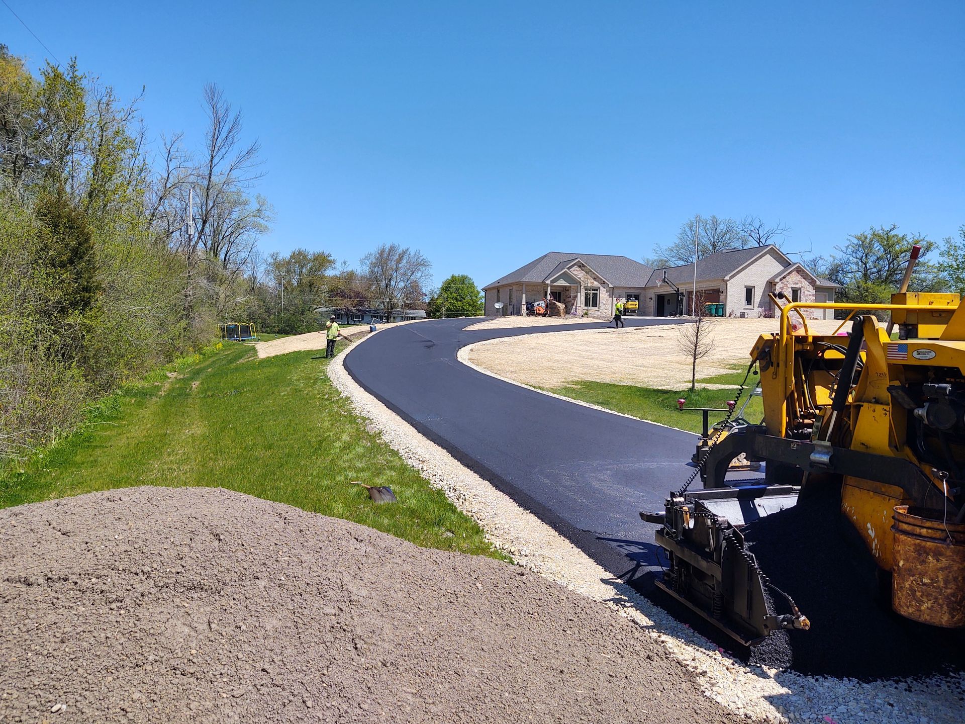 A yellow tractor is paving a road in front of a house.