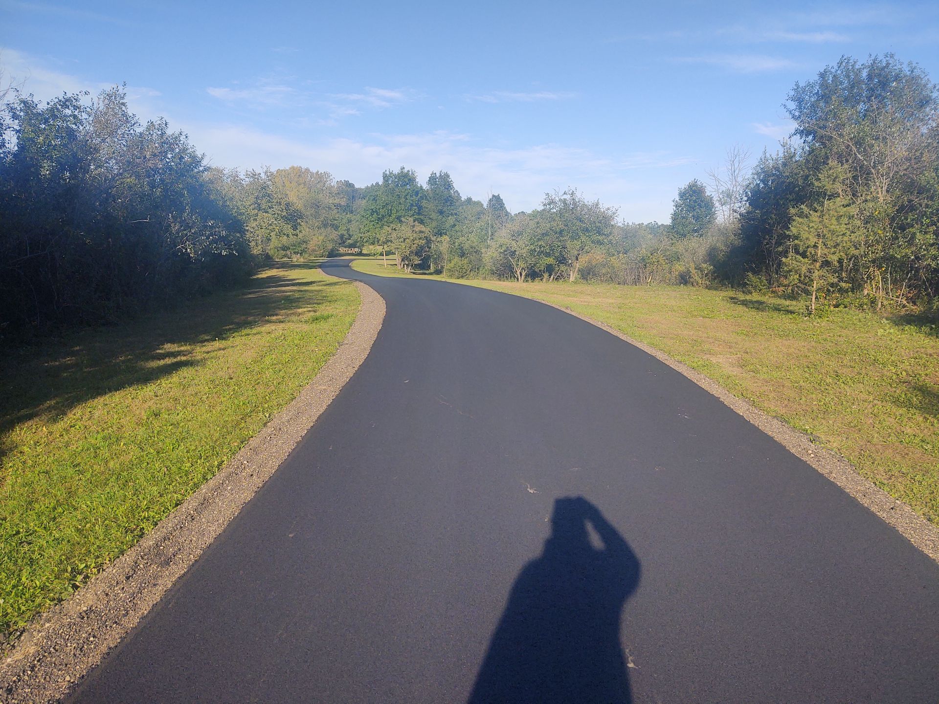 A person is taking a picture of their shadow on a road.