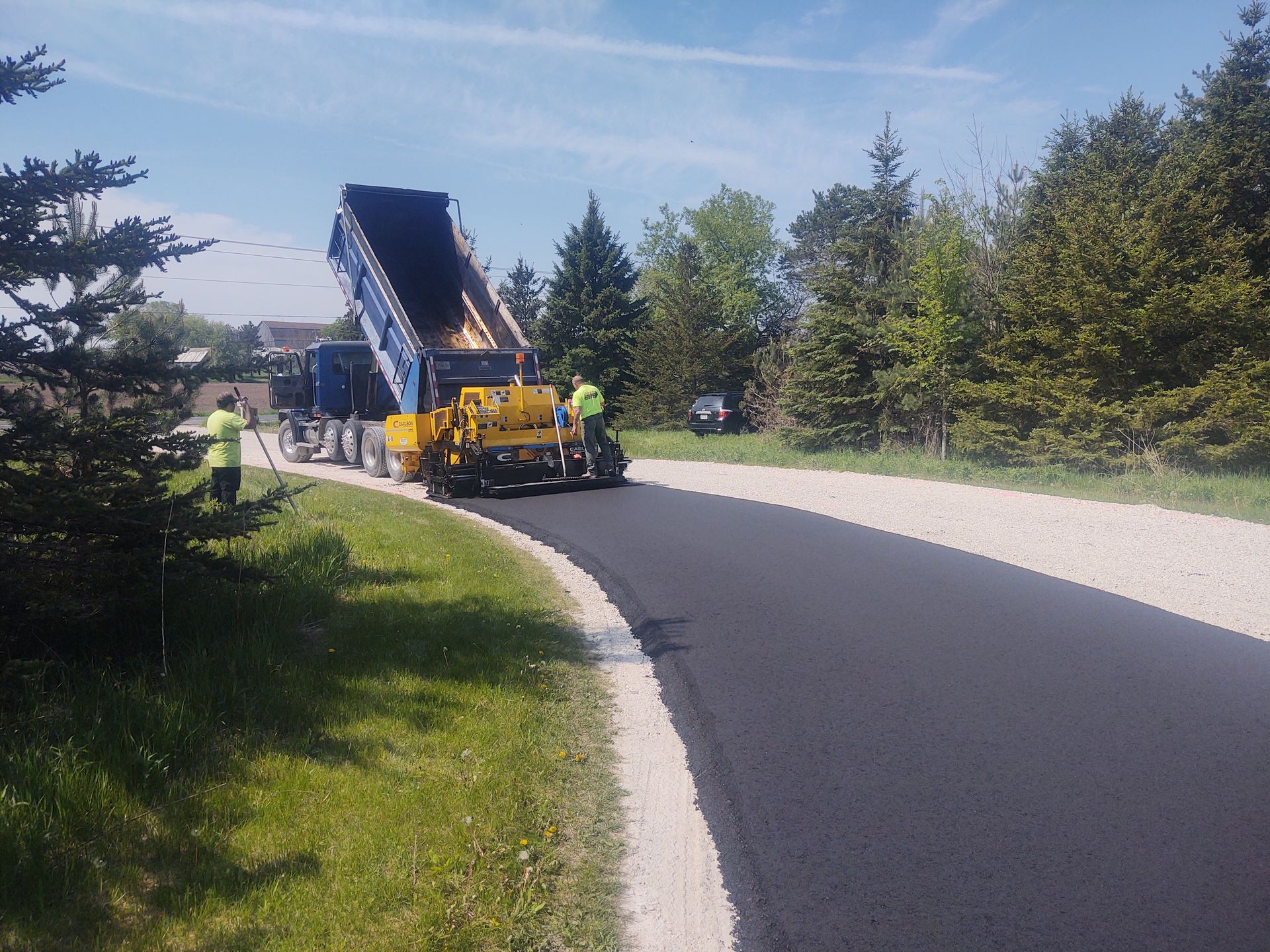 A dump truck is being loaded with asphalt on a curvy road.