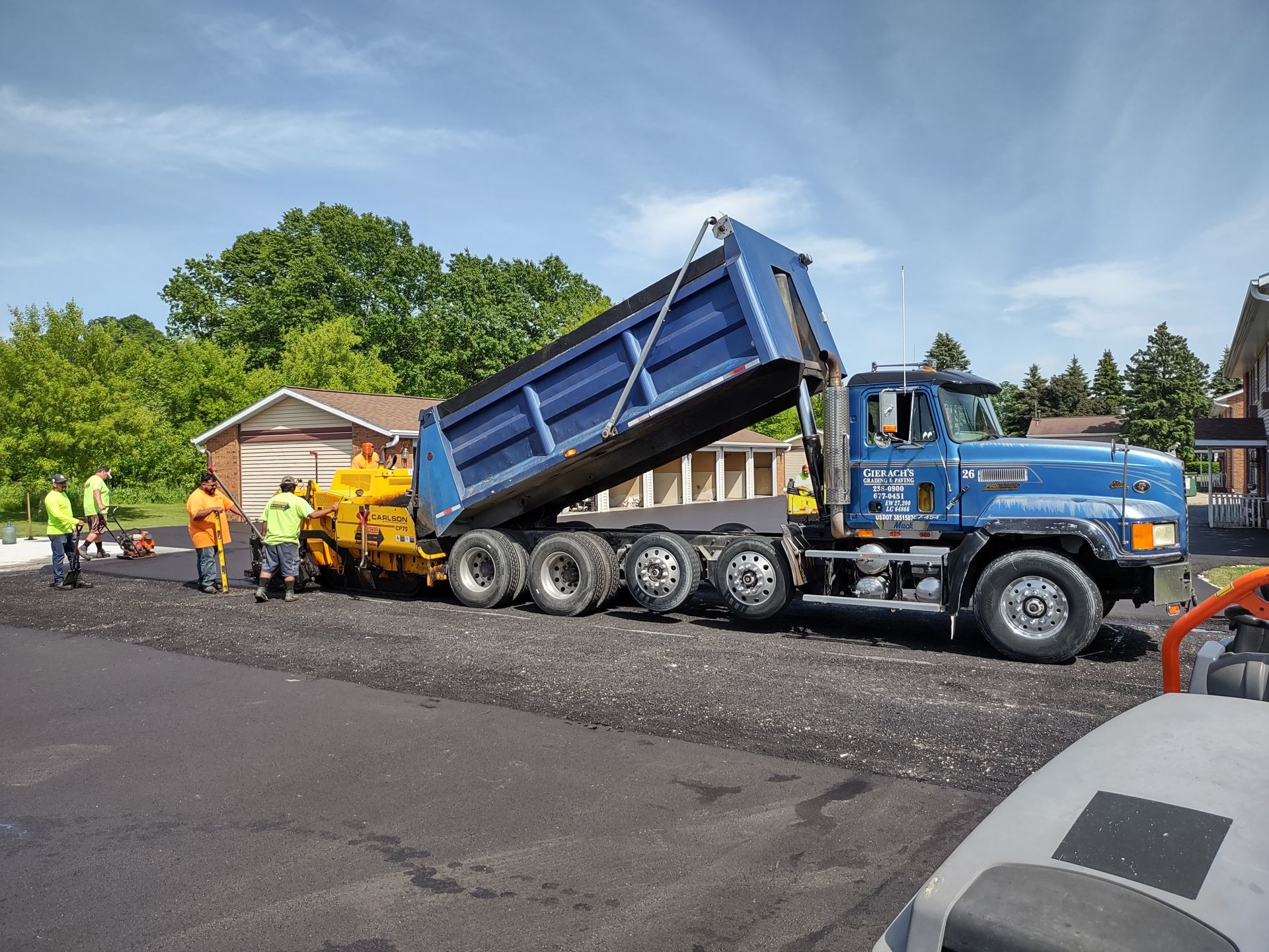 A dump truck is being loaded with asphalt on a construction site.