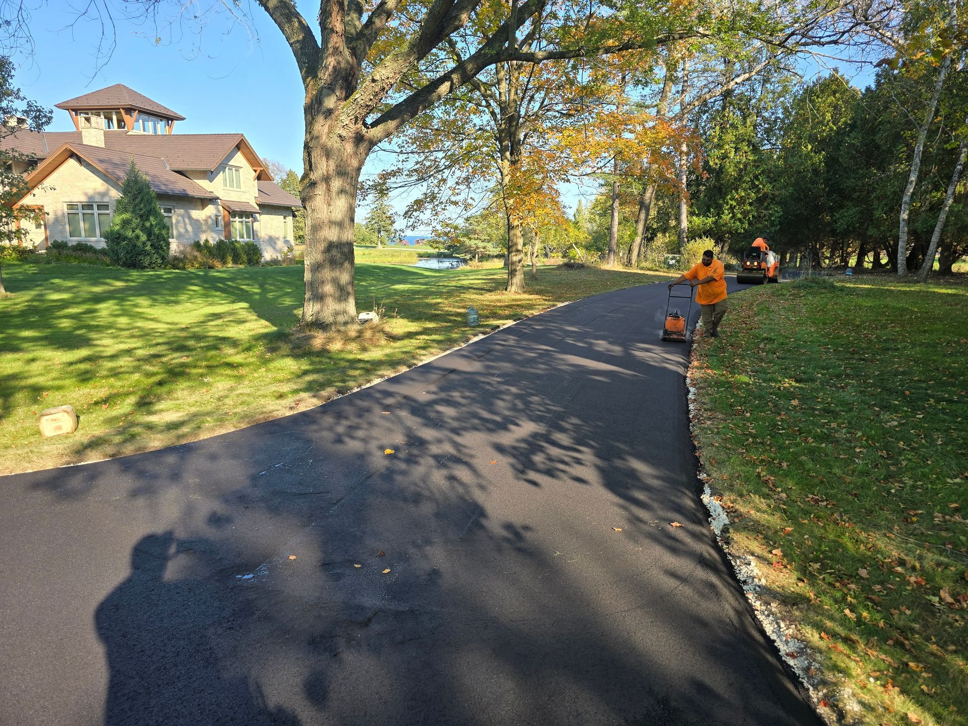 A man is cutting grass on the side of a road in front of a house.