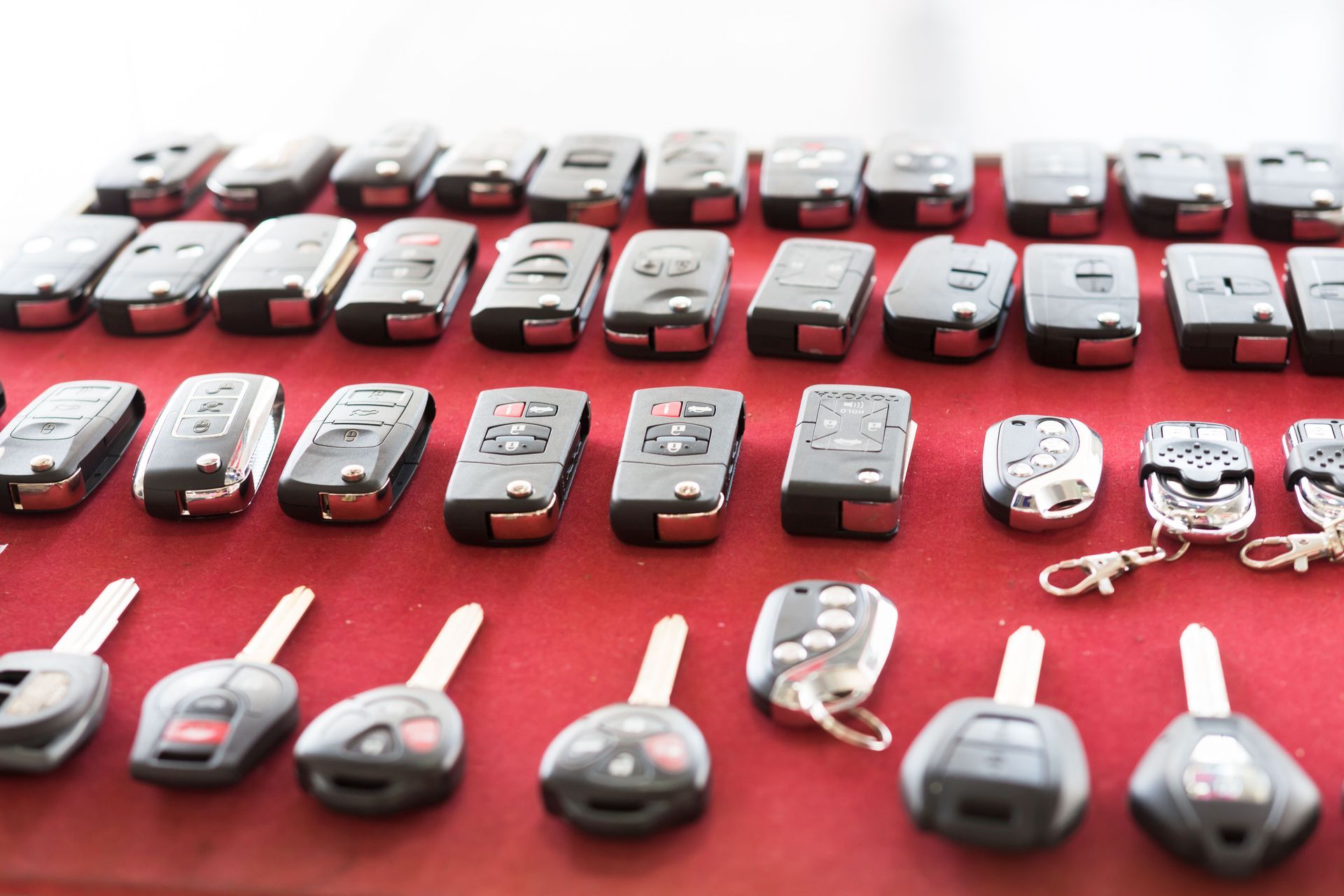 Rows of car keys and fobs on a red surface, showcasing various designs and styles.