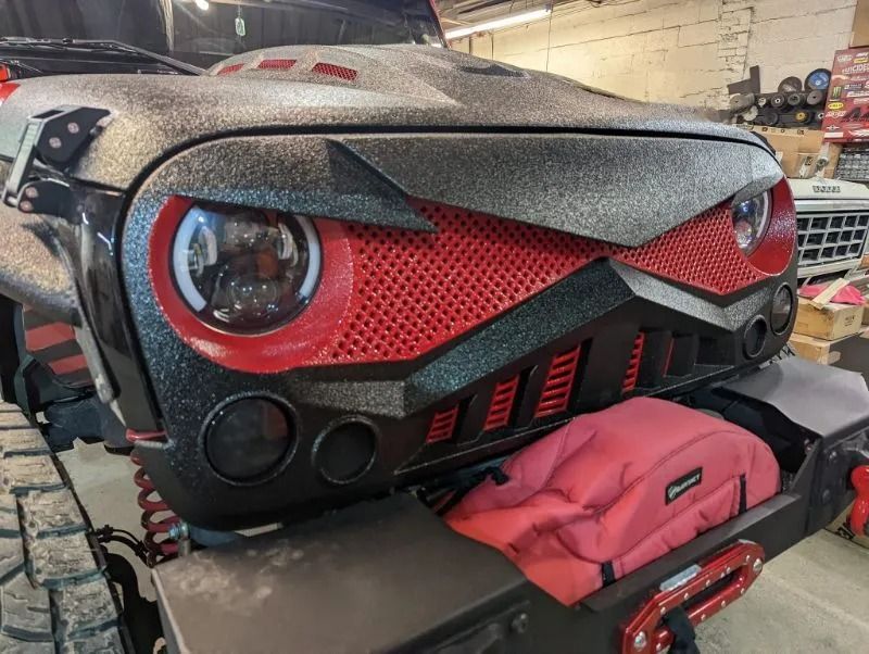 Red-and-black custom car front in a workshop, with a red bag resting on the bumper