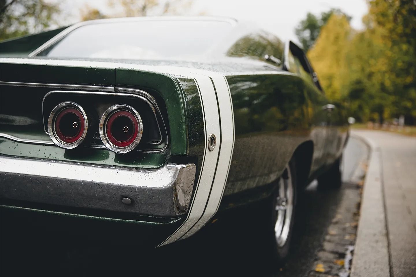 Classic dark green muscle car rear parked on a roadside, with twin round taillights and chrome trim.