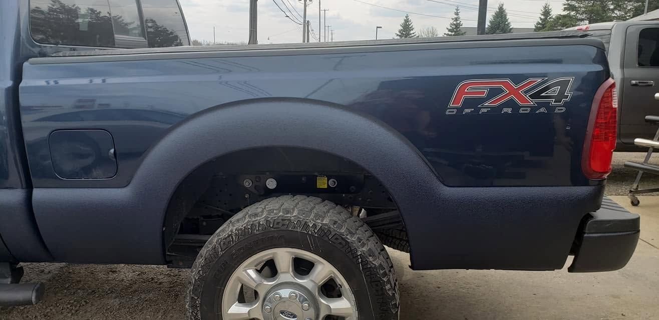 Dark blue pickup truck side view with FX4 decal and off-road tires parked outdoors