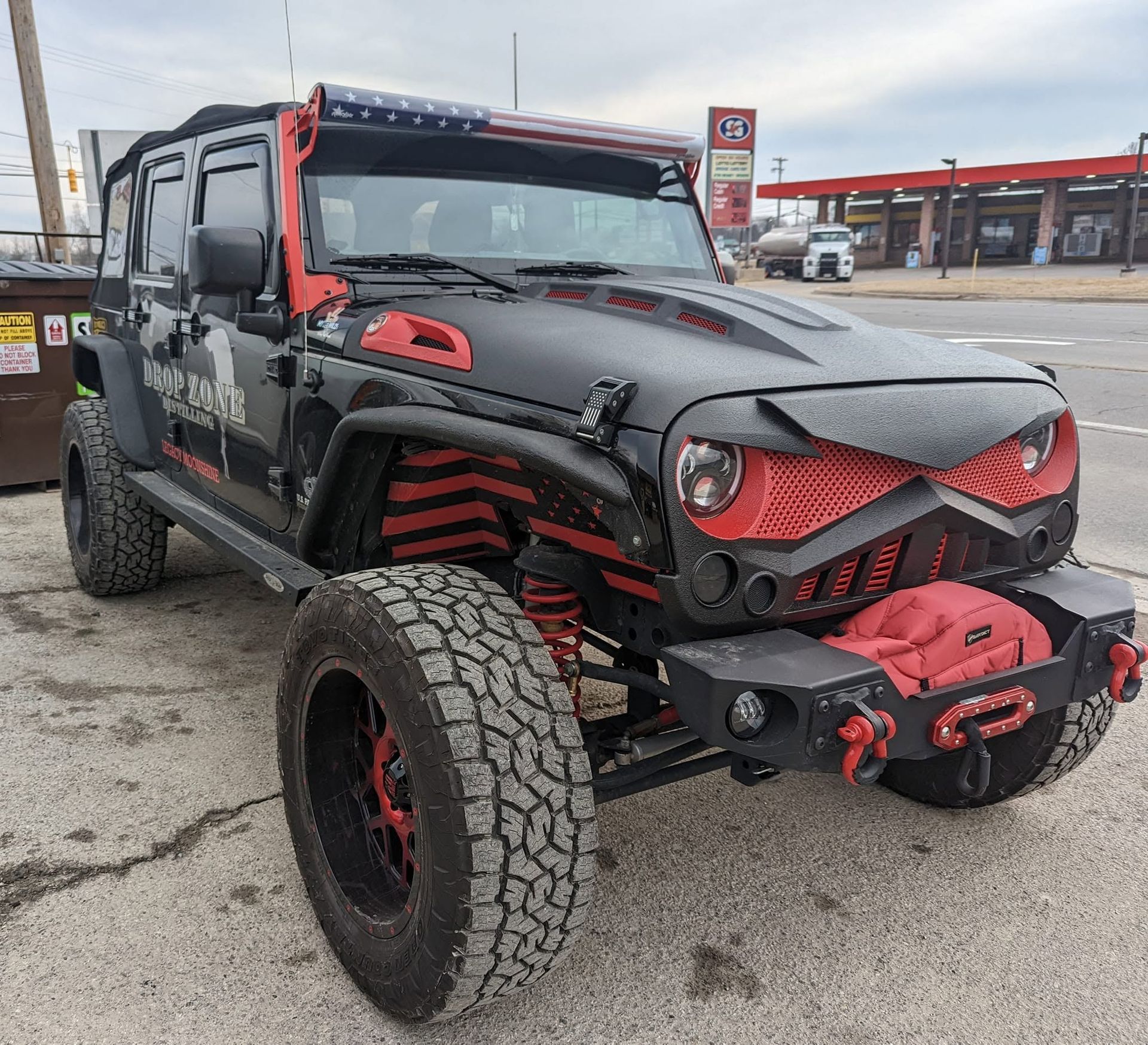Custom black-and-red lifted off-road truck parked at a gas station, with oversized tires and front winch