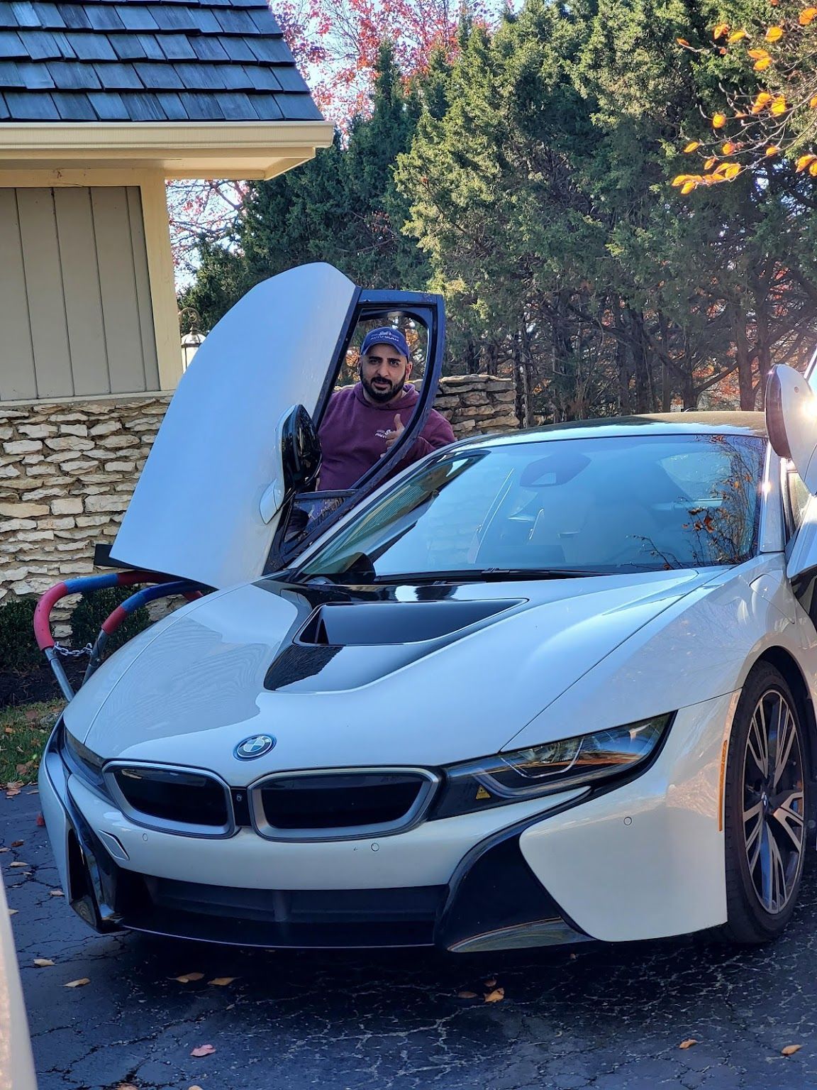 A man is standing next to a white bmw i8 with its hood open.